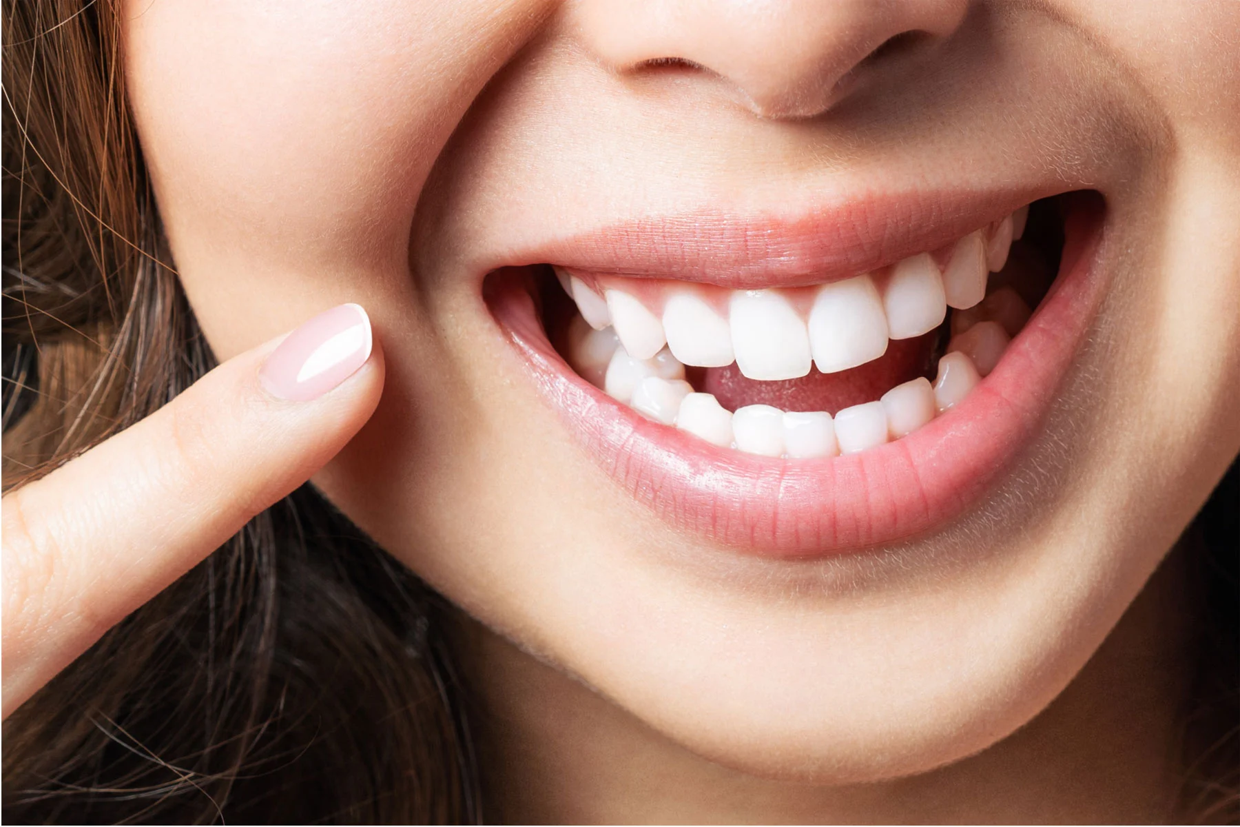 Close-up of a smiling woman pointing at her bright white teeth, showing confidence and healthy smile.