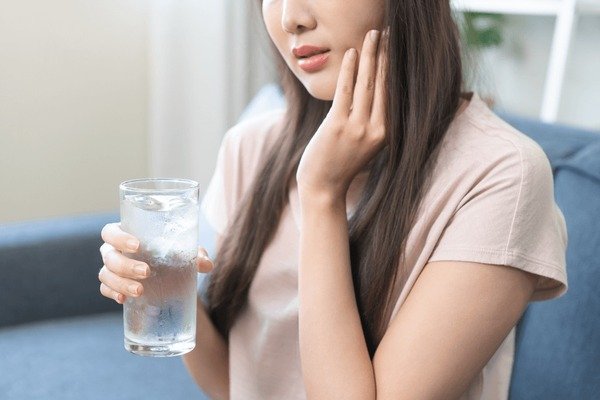 Person experiencing sharp tooth pain while drinking cold water