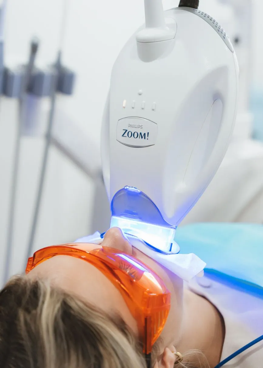 Patient undergoing professional Philips Zoom teeth whitening with LED light at dental clinic.