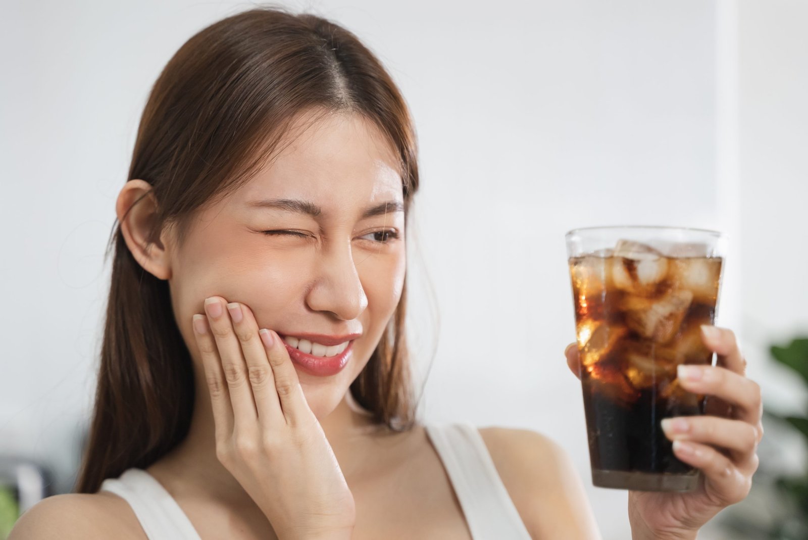 Young adult experiencing tooth sensitivity while drinking a cold beverage